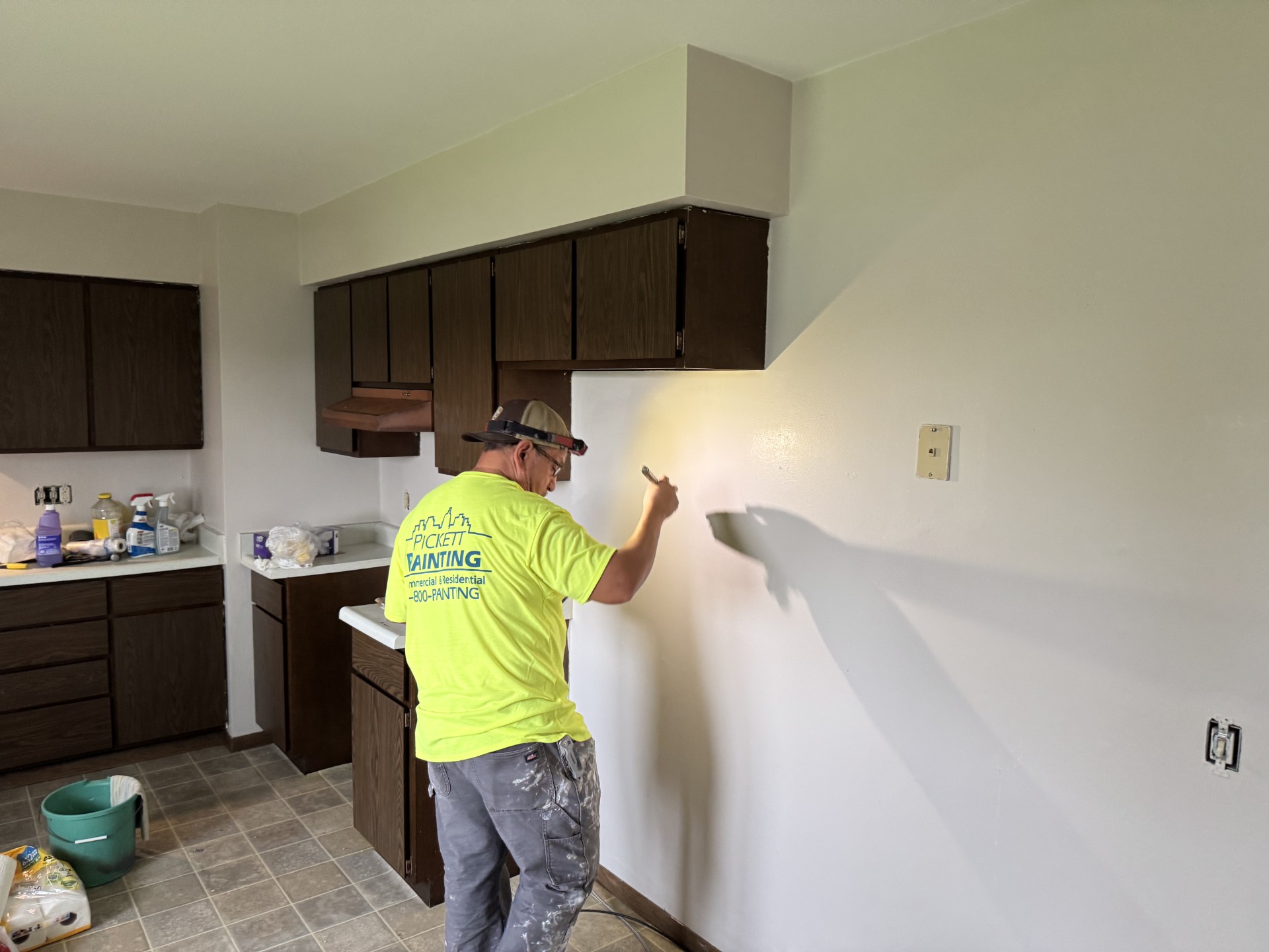A painter is painting a wall in an unfinished kitchen